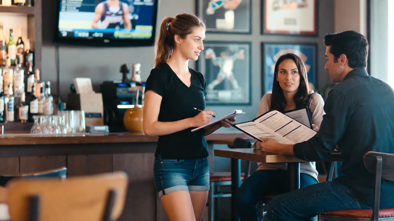 A young server with a notepad taking an order from a couple